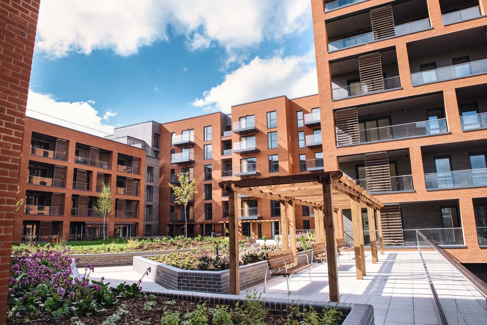 Brick apartment blocks with balconies around the landscaped courtyard at Halton Court, with a timber pergola and raised planters