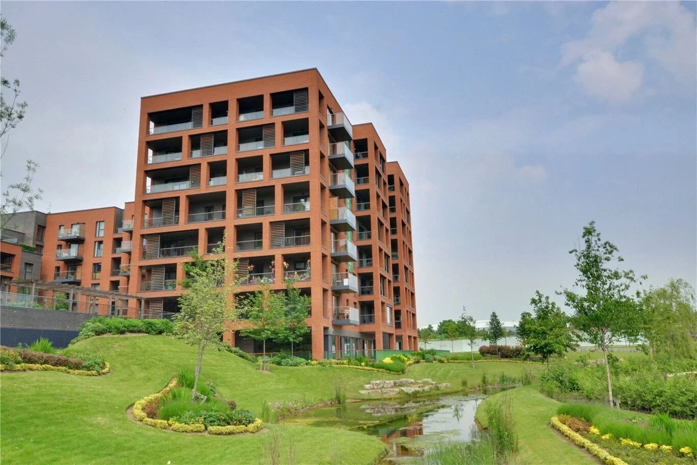 The red-brick Halton Court apartment block rising above landscaped lawns and a stream at Kidbrooke